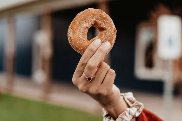 A person holding up a sugar-coated doughnut, likely enjoyed as part of the 'A Taste of Amish Country' experience.