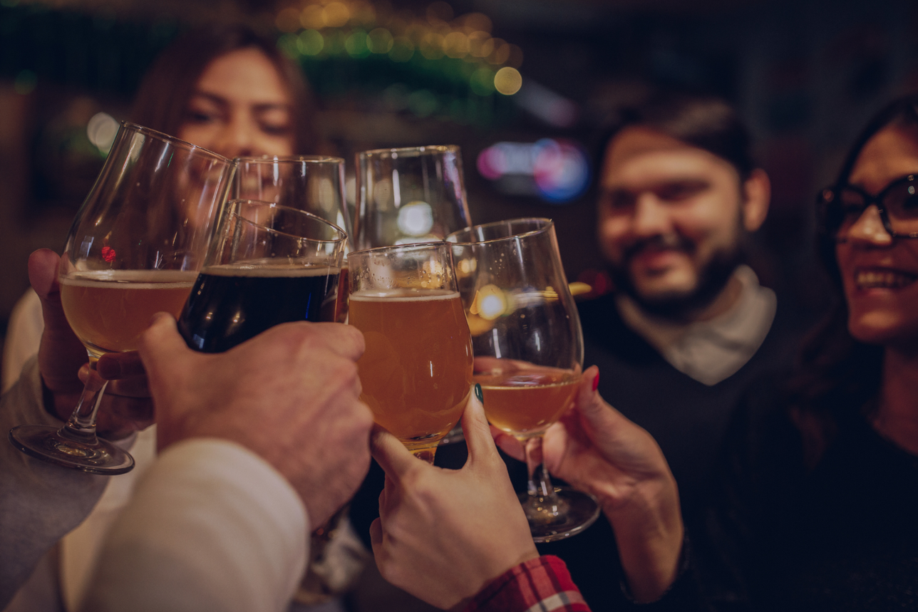 A group of people toasting with glasses of beer and wine at a social gathering, with blurred faces for privacy.