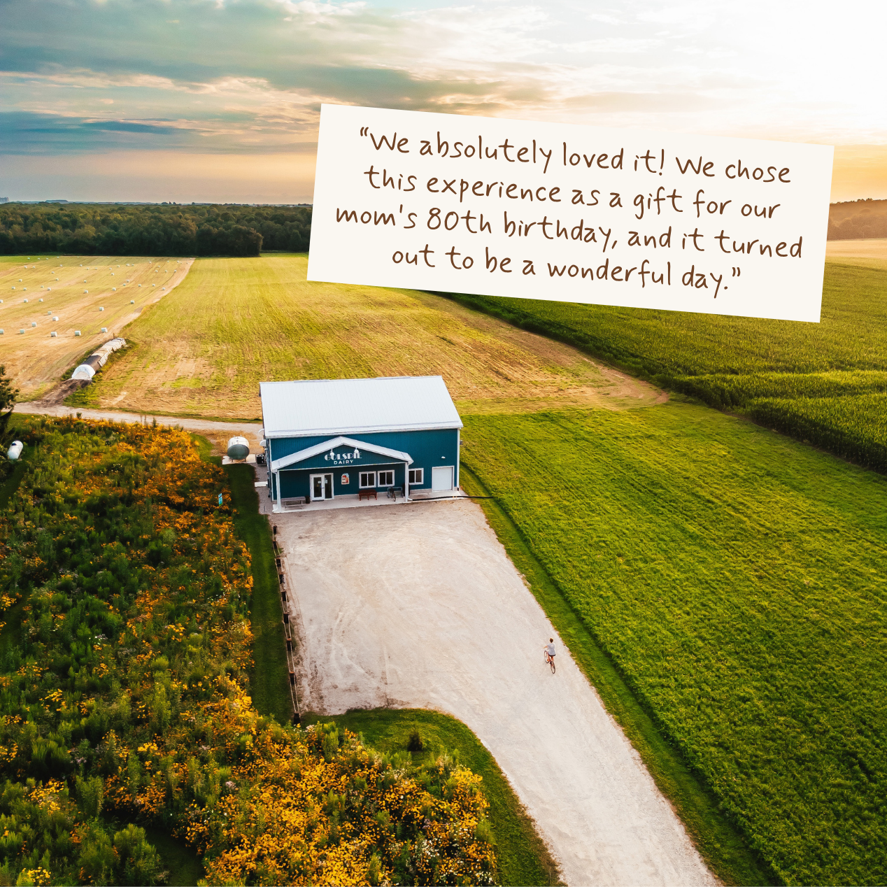 Aerial view of a blue farmhouse surrounded by green fields and trees, with a large handwritten note overlaid near the top right reading, 'We absolutely loved it! We chose this experience as a gift for our mom's 80th birthday, and it turned out to be a wonderful day.'.