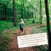 A woman hiking on a forest trail viewed from behind, carrying a blue backpack and trekking poles. A cream-colored paper note with a customer review is placed in the lower right corner of the image.