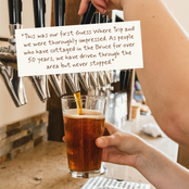 A person holds a pint of amber beer under a draft tap, with a handwritten note overlaid near the top. The scene appears to be in a bar or pub environment.