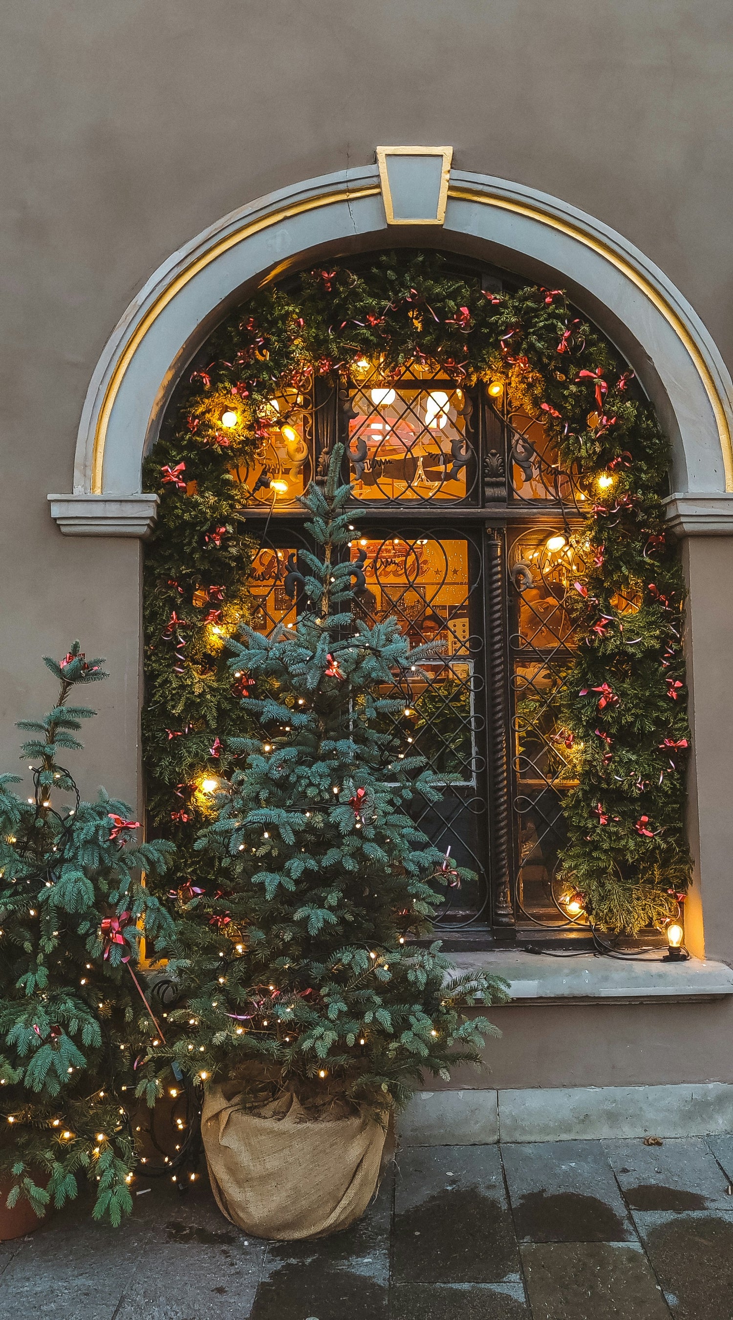 Decorative Christmas trees and lights in front of a building entrance with an archway.