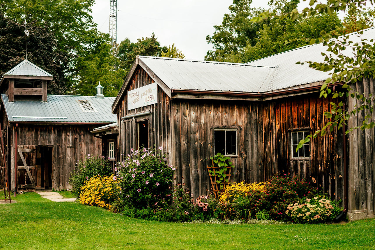 Old wooden barn with a garden in front, surrounded by trees