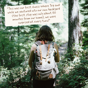 A woman seen from behind wearing a large gray and brown hiking backpack, standing on a forest path with a handwritten note overlaid in the top left corner.
