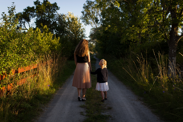 Mother and child walking on a winding road surrounded by greenery