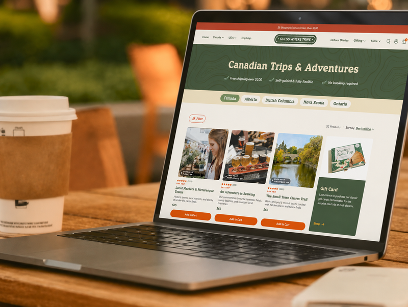 A laptop on a wooden table showing a website for Canadian trips and adventures, with a takeaway coffee cup nearby and a blurred outdoor background.