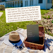 A picnic-style outdoor scene with a straw hat, blue visor, white sunglasses, a woven basket, and a book titled "Guess Where You'll Go" placed on a blanket. A handwritten note is overlaid near the top, and the background shows a real outdoor setting with grass, flowers, and a house.
