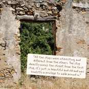 A square photo print or card featuring a scenic view of ancient stone ruins with a quote overlaid in a handwritten brown font on a white background.