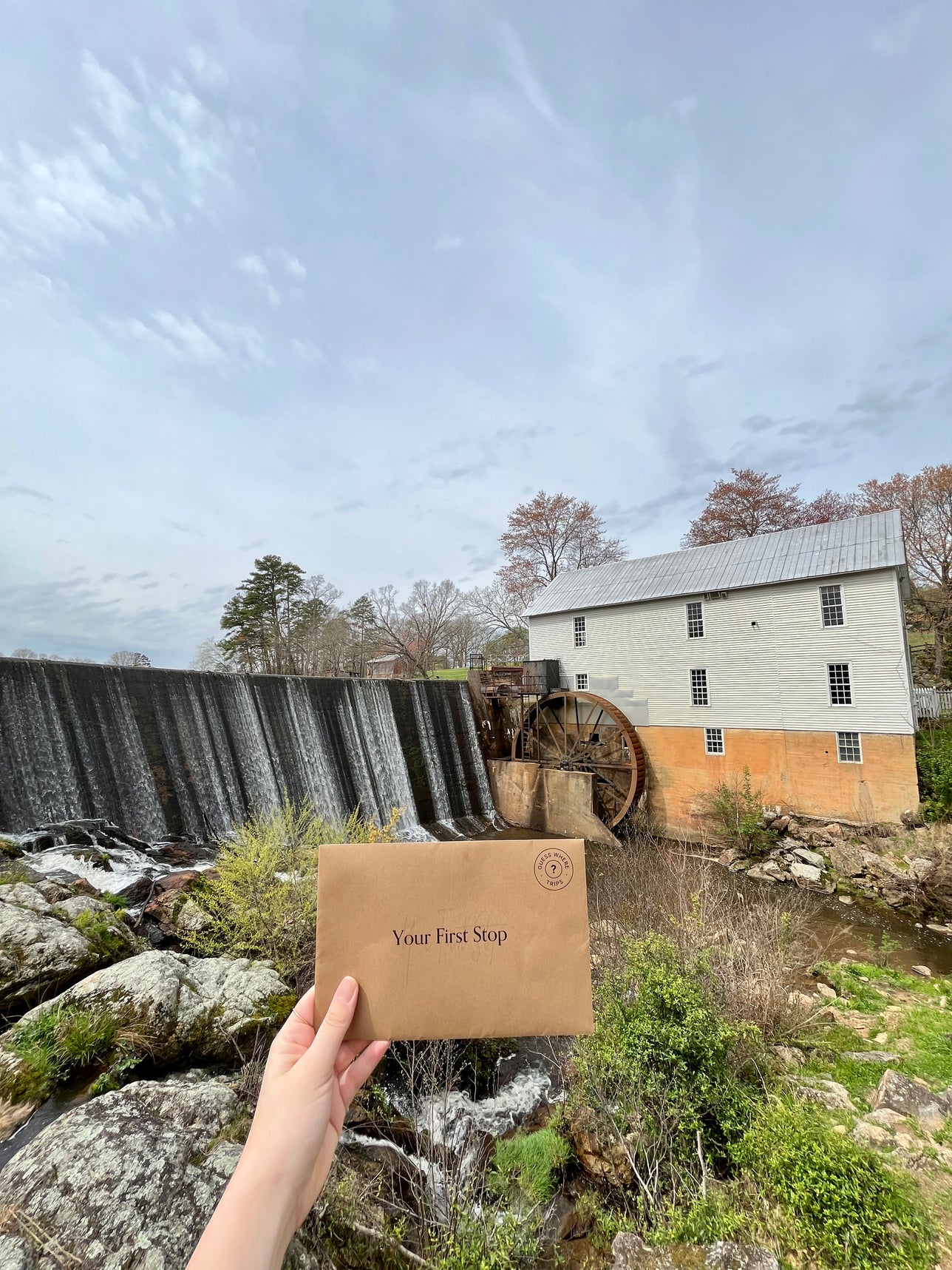 Hand holding up a first stop envelope in front of a waterfall and historic building