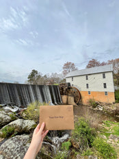 Hand holding up a first stop envelope in front of a waterfall and historic building