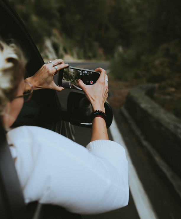 A person taking a photo with a smartphone from a car, capturing a scenic view.