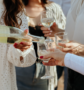 Person pouring a wine bottle into a wine glass for a group of people