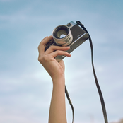 Hand holding up a vintage camera in front of a blue sky