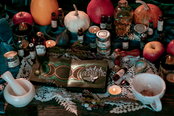 A thematic setup featuring items related to witchcraft and Halloween, including pumpkins, candles, books, and various decorative elements on a table.