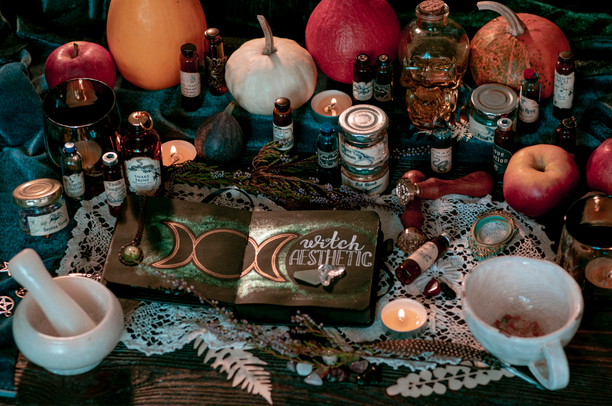 A thematic setup featuring items related to witchcraft and Halloween, including pumpkins, candles, books, and various decorative elements on a table.