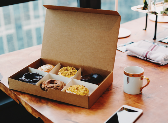 Box of six donuts on a wooden table.