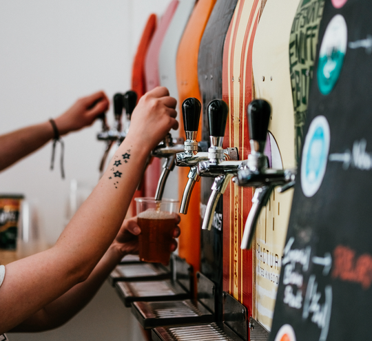Beers being pulled from taps on a colorful wall.