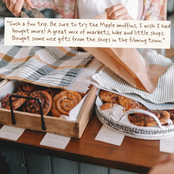 A styled bakery scene with trays of cinnamon rolls and muffins on a wooden table, with a person's hands holding a brown paper bag in the background. A handwritten quote card is placed on the table.