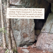 A review with brown text on a cream background is superimposed over a natural outdoor scene showing large gray boulders and tree trunks in a forest.