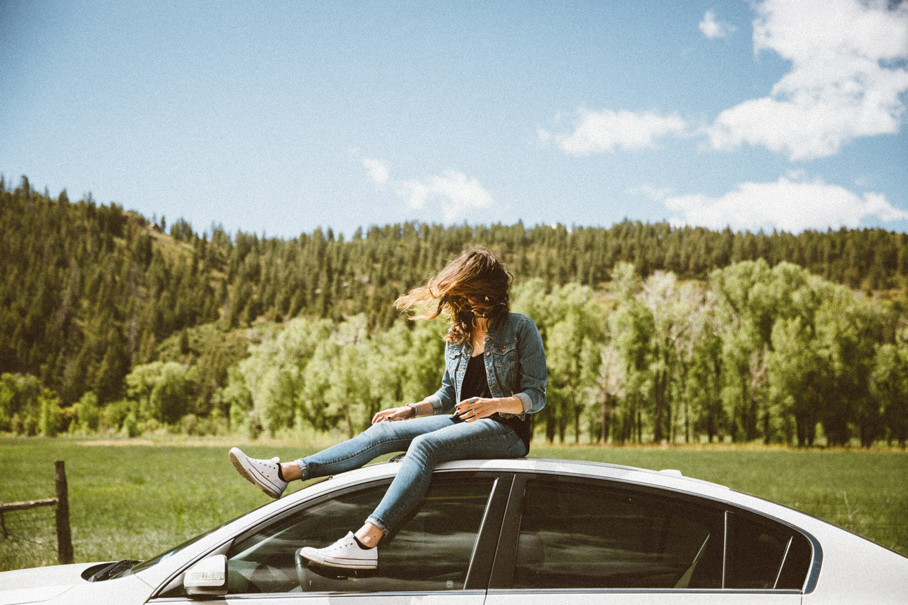 Woman sitting on top of parked car.