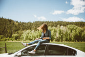 Woman sitting on top of parked car.