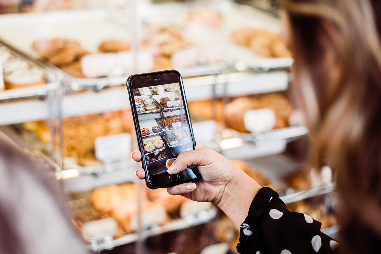 Woman taking video of bakery display with phone.