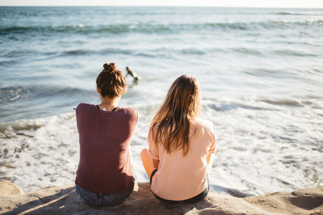 Two woman sitting on rocks by ocean.