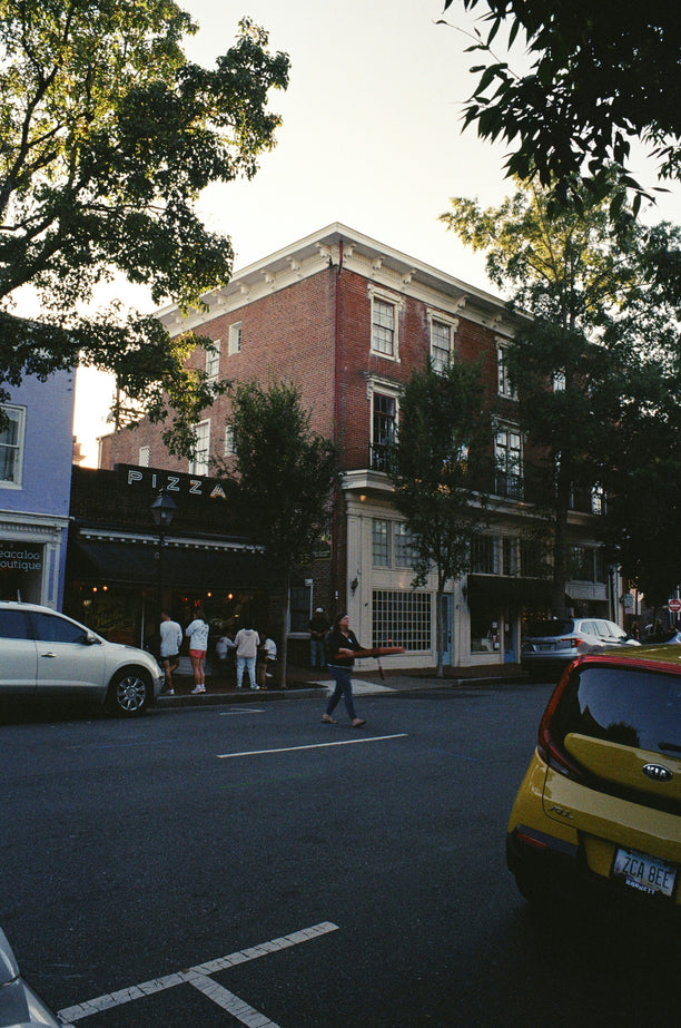 A street scene in a city with trees, buildings, and cars. People are walking on the sidewalk.