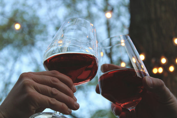 Two people clinking glasses of red wine.