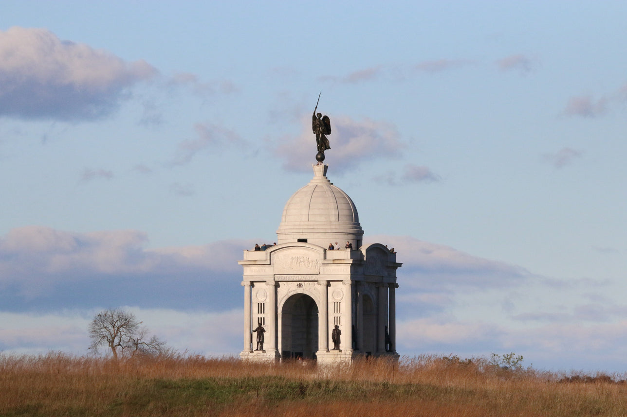 A monument at Gettysburg, featuring a statue on top of a classical Revival dome, surrounded by an open field under a partly cloudy sky.