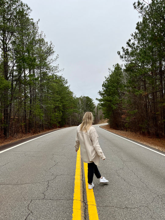 Woman standing with back to the camera, on a line in the middle of picturesque road.
