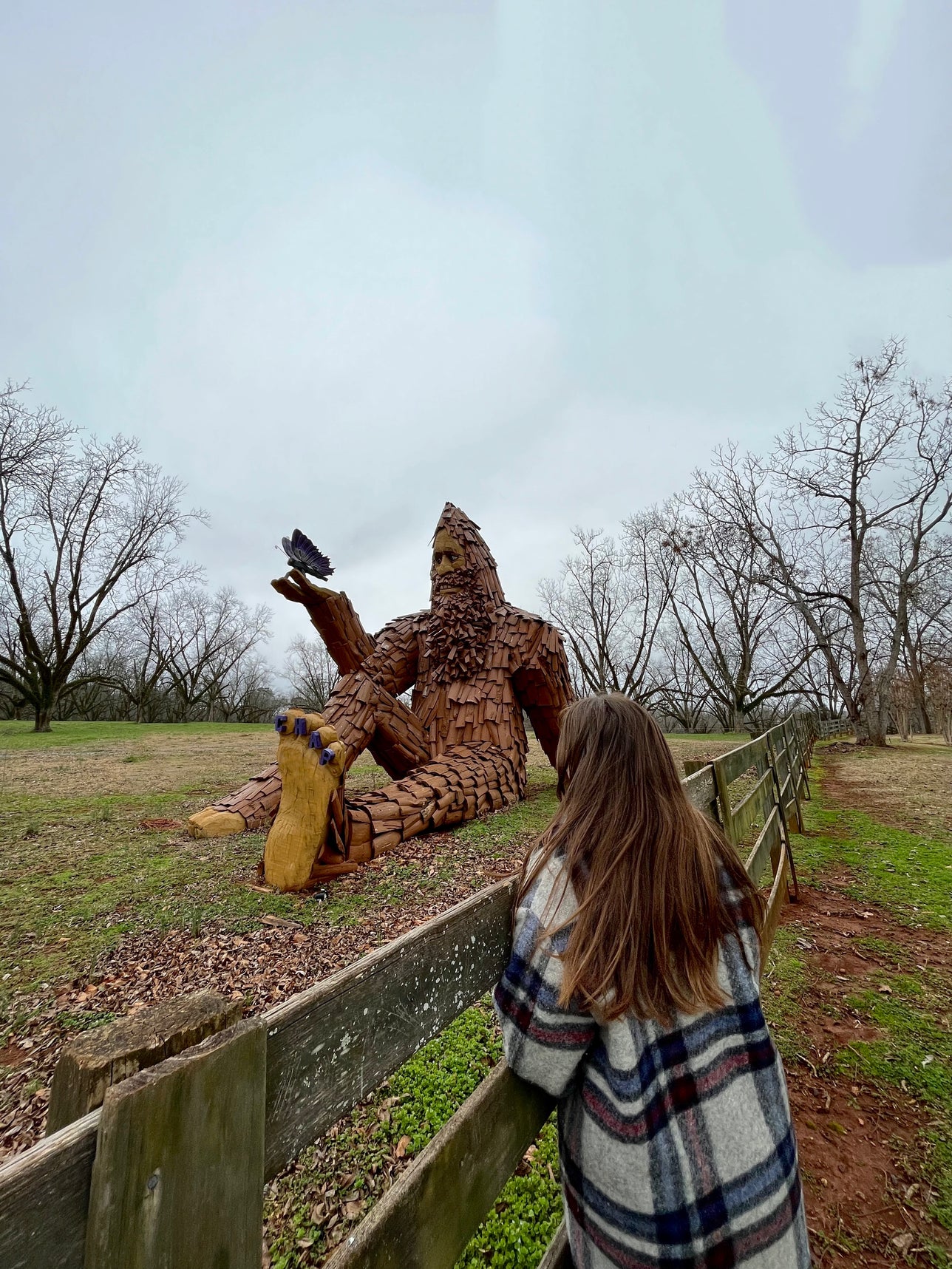 Woman looking at large Bigfoot carved from wood. 
