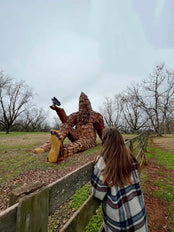 Woman looking at large Bigfoot carved from wood. 