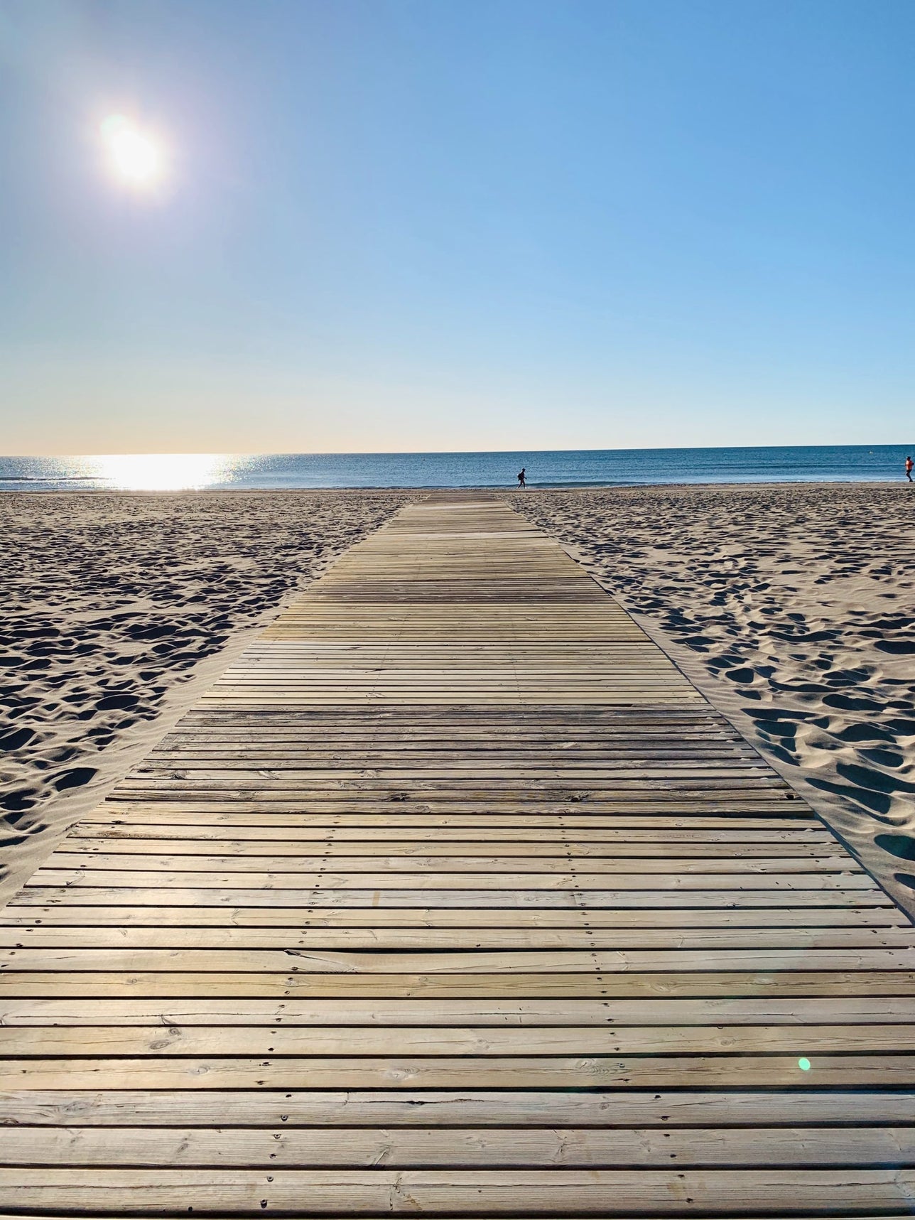 A boardwalk leading to a beach with the sun shining brightly in the sky.