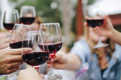 Group of friends clinking glasses full of red wine.