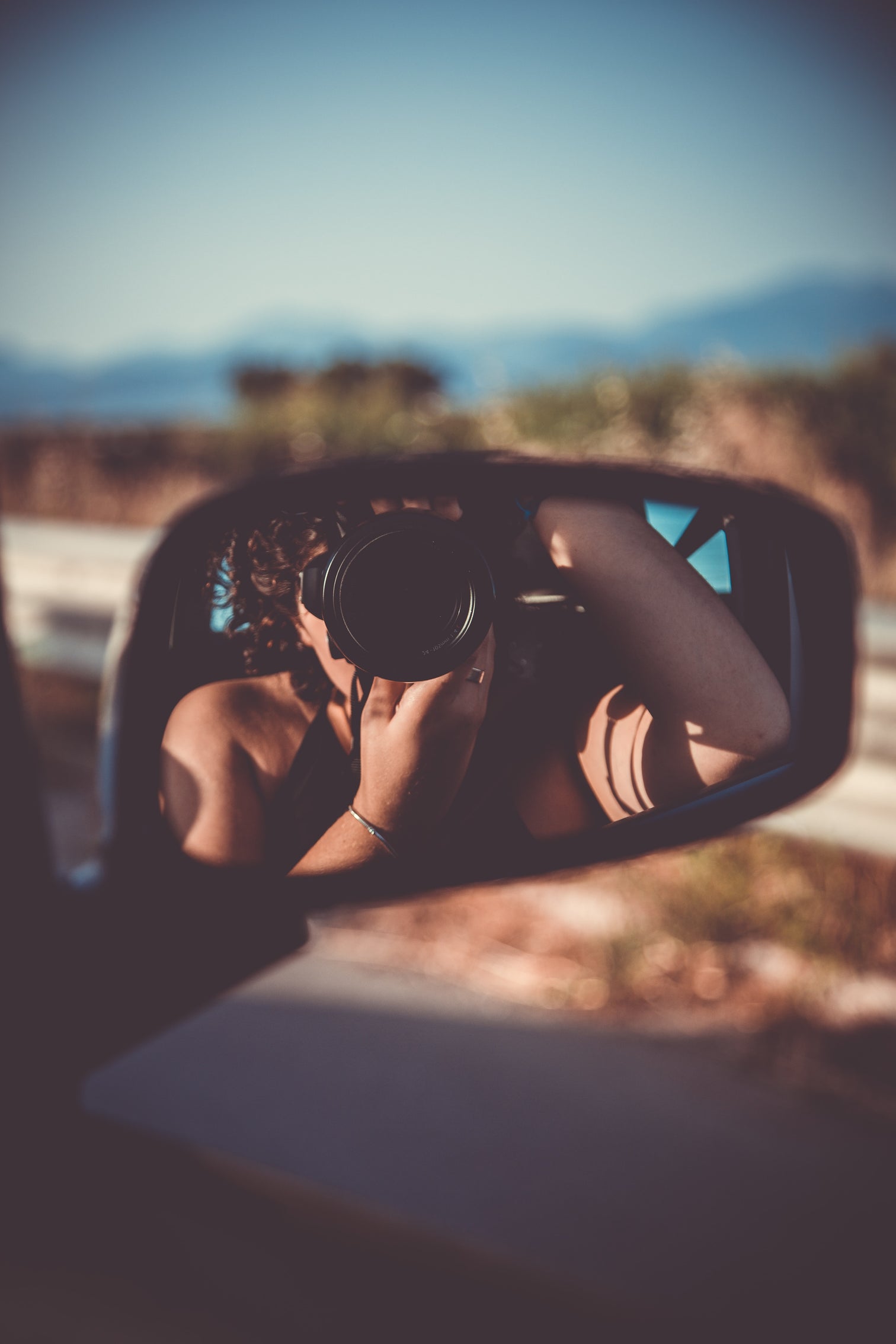 Woman taking photo can be seen in side view mirror of car.